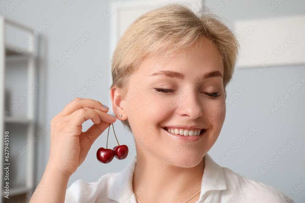 Beautiful happy young woman with ripe cherries in living room