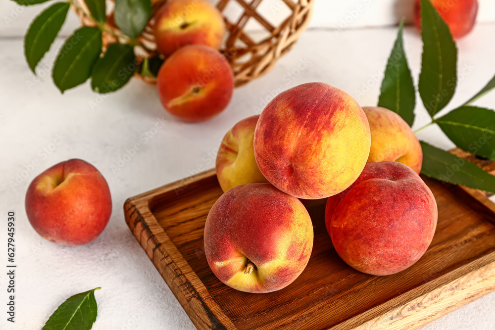 Wooden board with sweet peaches and leaves on white table