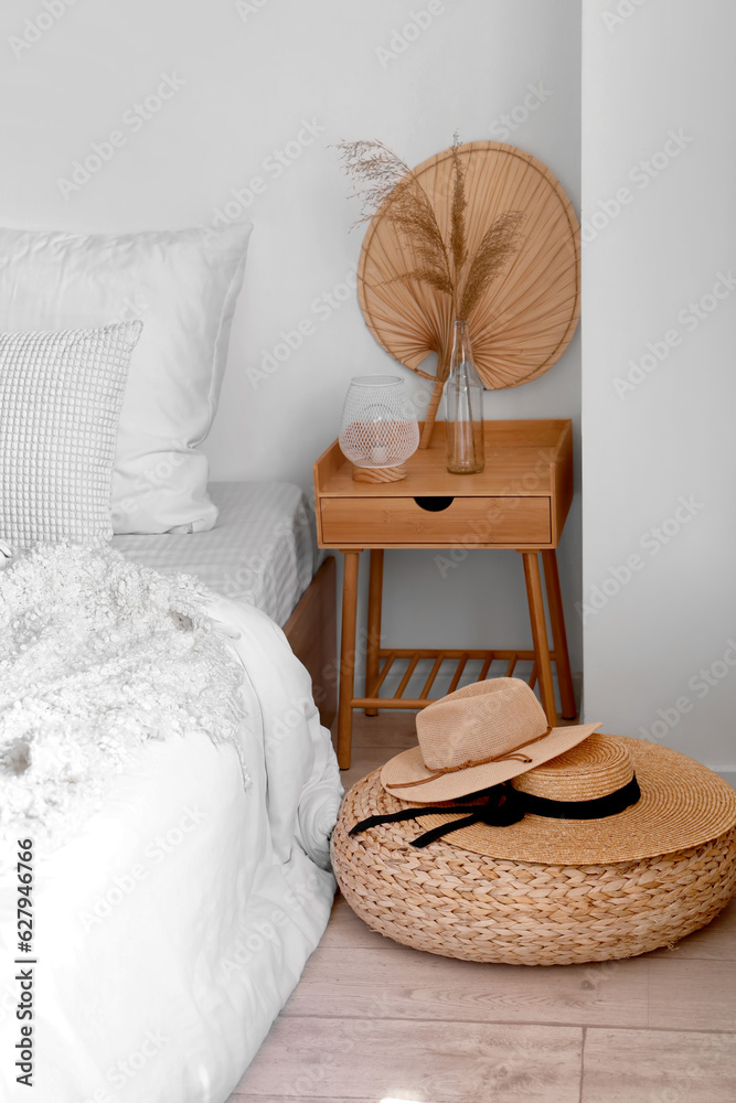 Cozy bed, bedside table and hats on wicker mat in bedroom