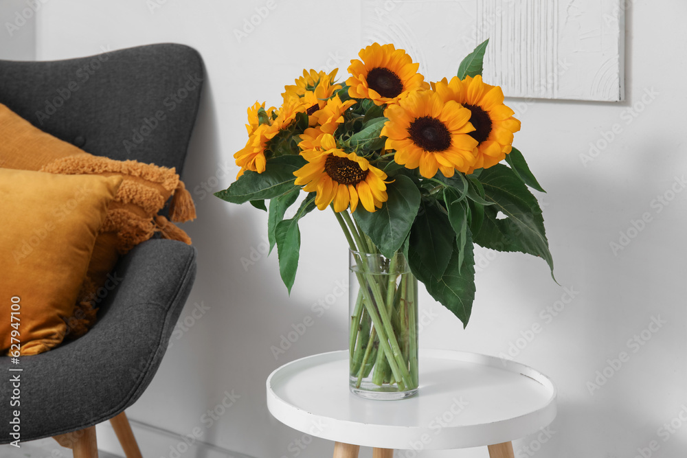 Vase with beautiful sunflowers on table near white wall