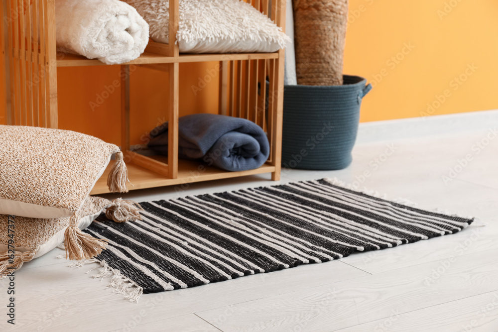 Stylish rug, cushions and shelving unit near orange wall