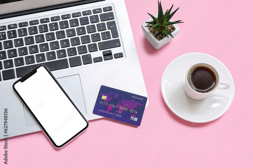 Laptop with credit card, cup of coffee and mobile phone on pink background