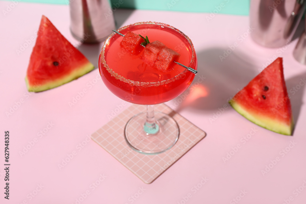 Glass of tasty watermelon cocktail with shakers on pink background