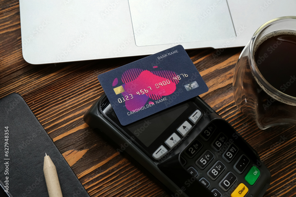 Laptop with payment terminal, cup of coffee and credit cards on brown wooden background