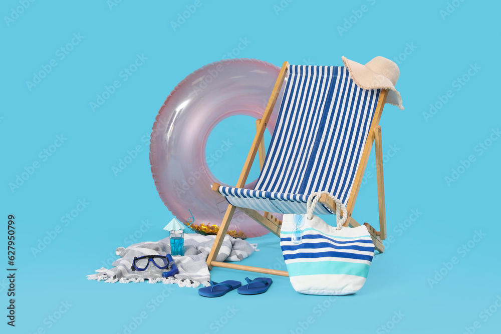 Deckchair, inflatable ring and glass of cocktail on blue background