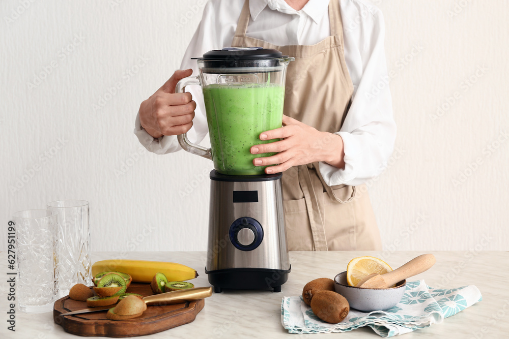 Woman preparing fresh kiwi smoothie in kitchen