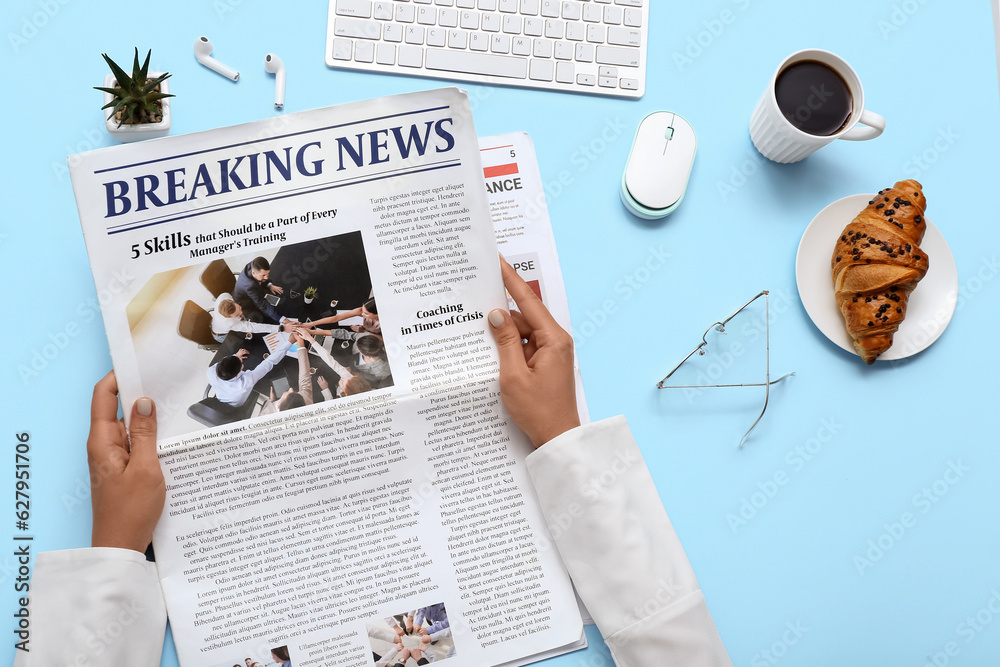 Woman reading newspaper at workplace with coffee and croissant on blue background