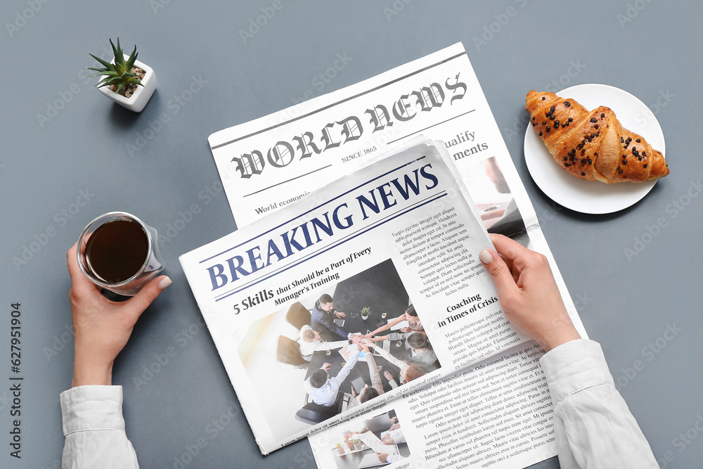 Woman reading newspaper with coffee and croissant on grey background