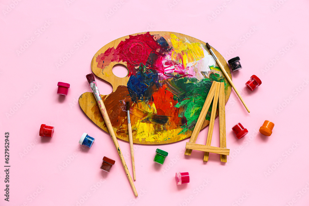 Palette with brushes and paints on pink background