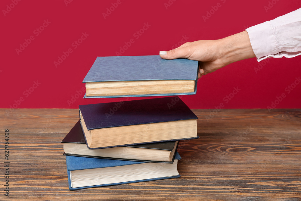 Female hand taking book on wooden table against red background