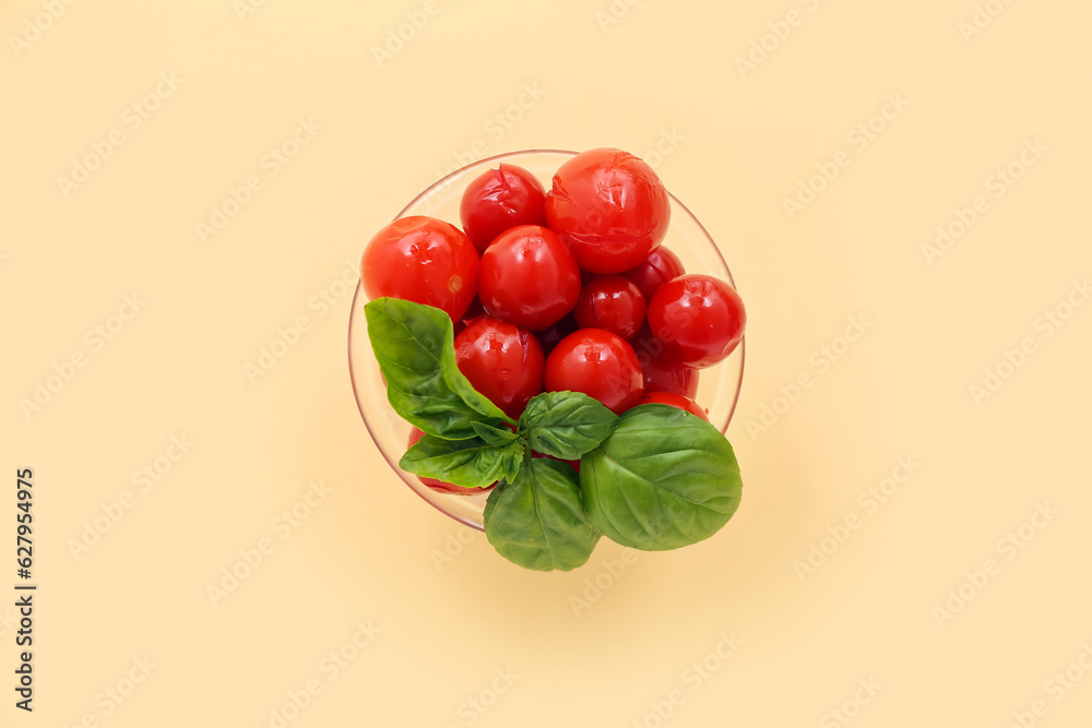 Glass bowl with canned tomatoes and basil on yellow background