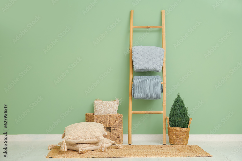 Ladder with blankets and cushions near green wall