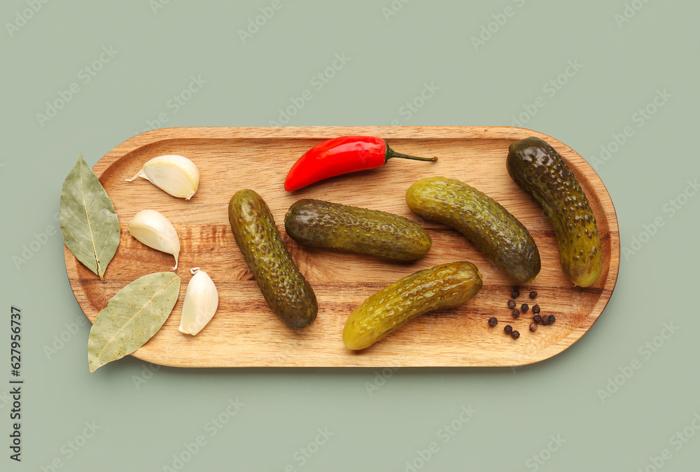 Wooden board with pickled cucumbers and different spices on green background