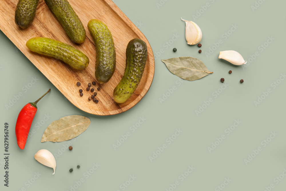 Wooden board with pickled cucumbers and different spices on green background