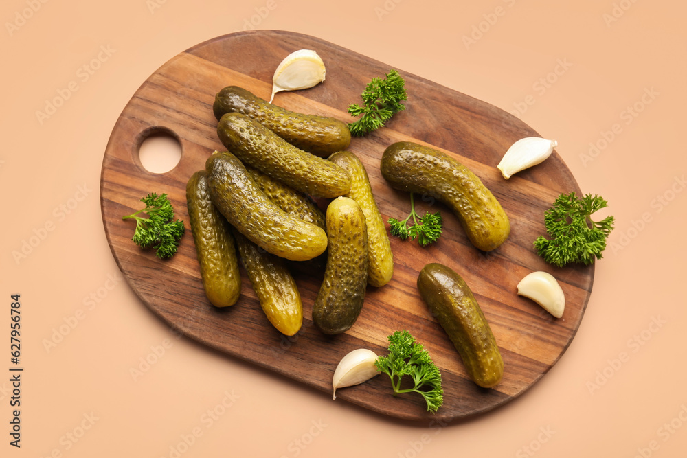 Wooden board with pickled cucumbers, parsley and garlic on orange background