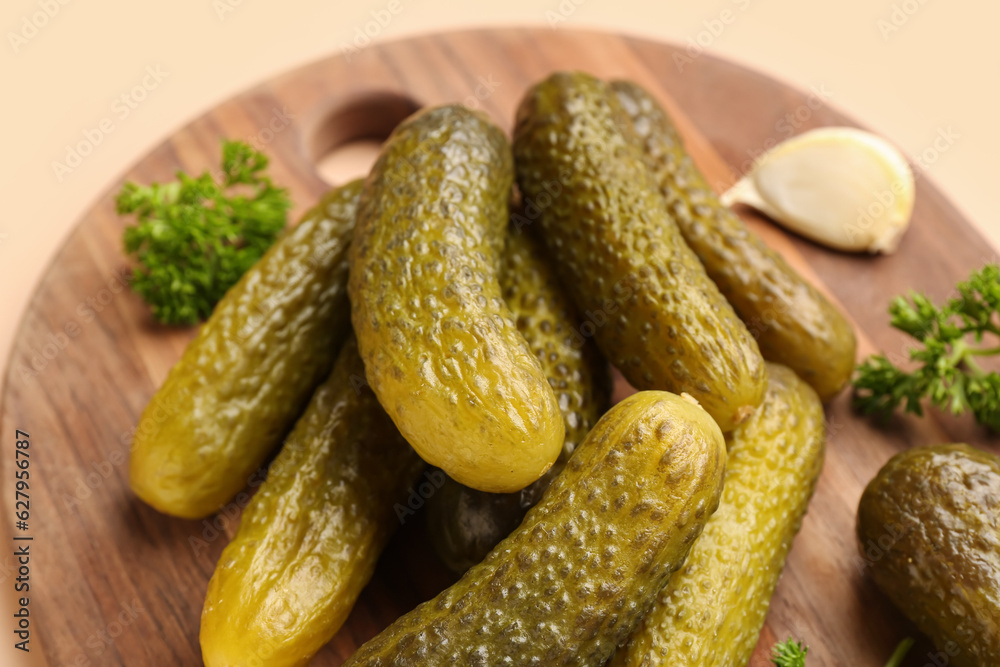 Wooden board with pickled cucumbers, parsley and garlic on orange background