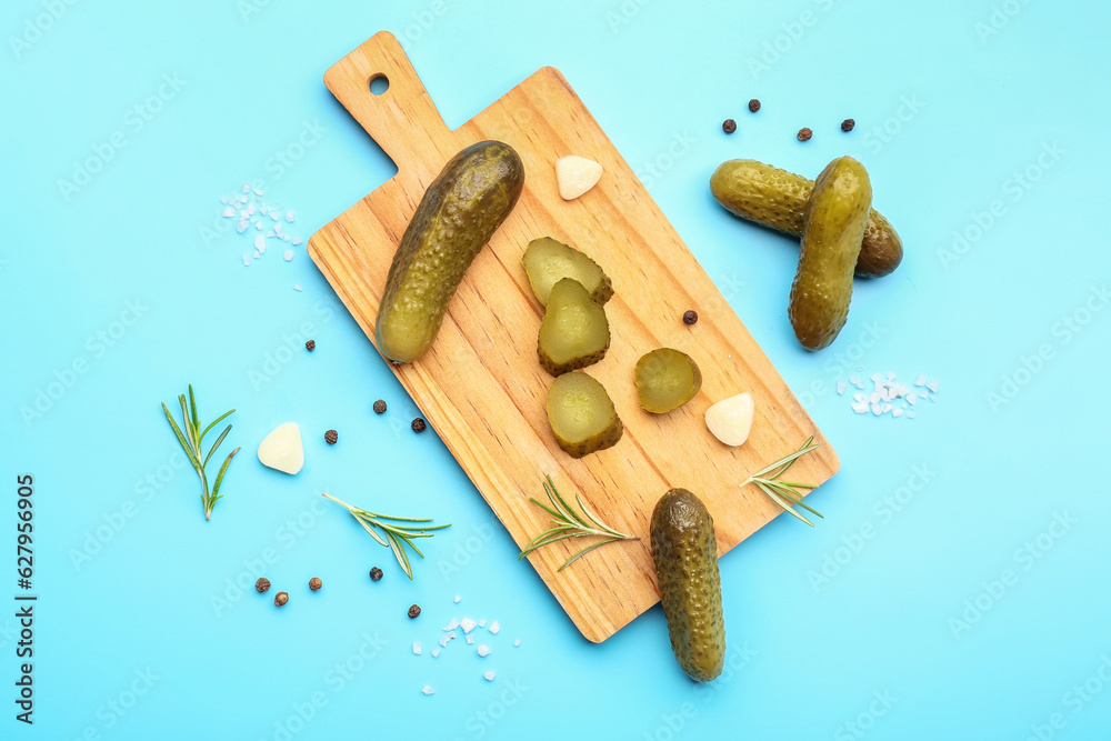 Wooden board with pickled cucumbers and different spices on blue background