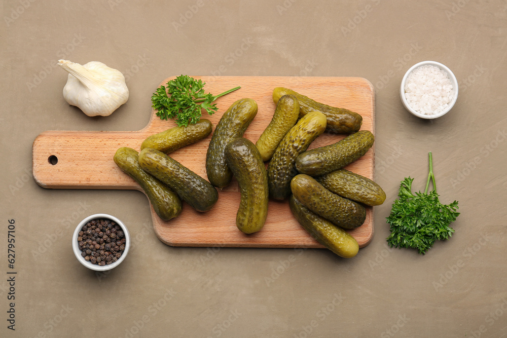 Wooden board with pickled cucumbers and different spices on brown background