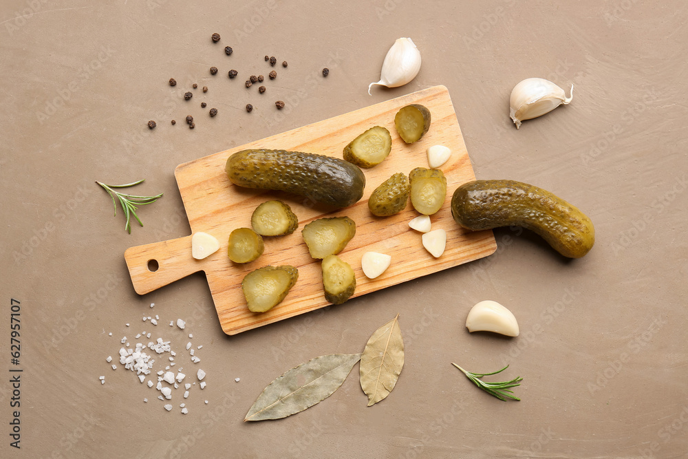 Wooden board with pickled cucumbers and different spices on brown background