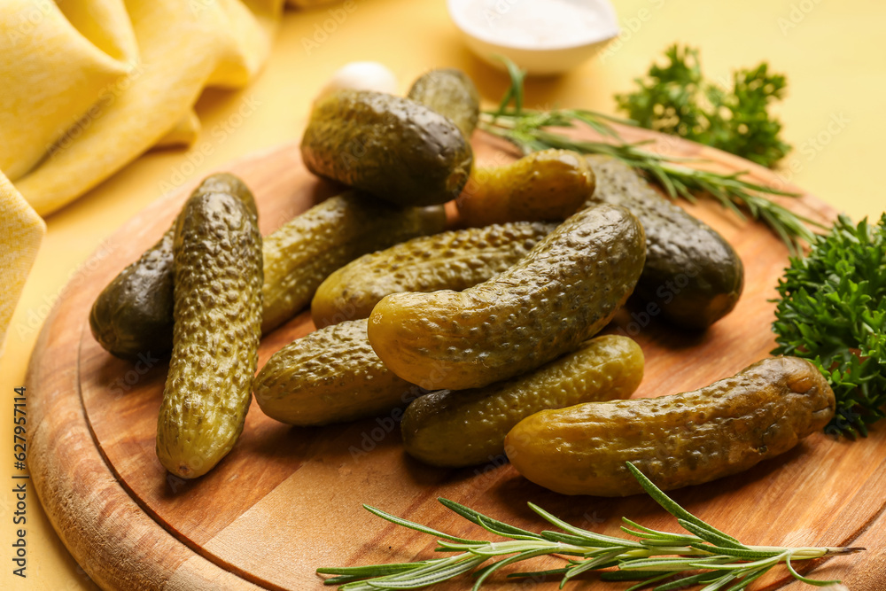 Wooden board with pickled cucumbers, rosemary and parsley on yellow background