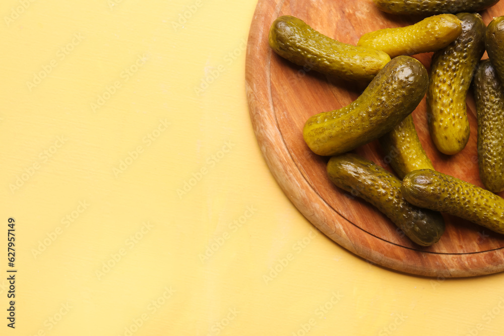 Wooden board with pickled cucumbers on yellow background