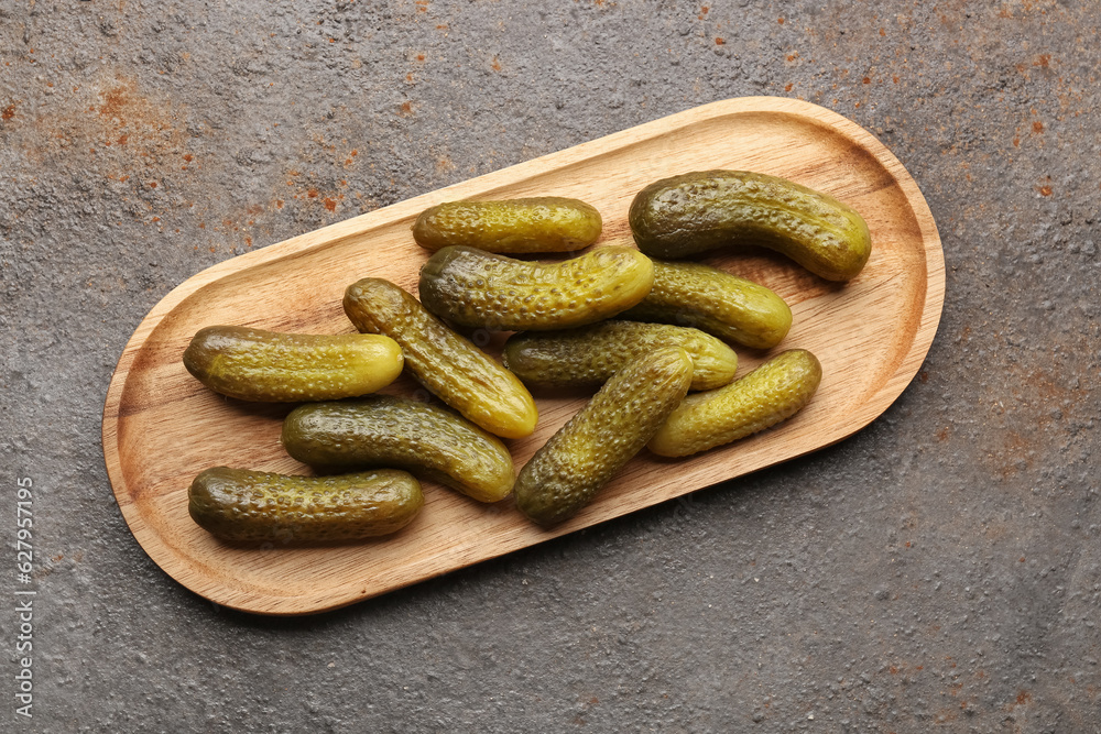 Wooden board with pickled cucumbers on dark background