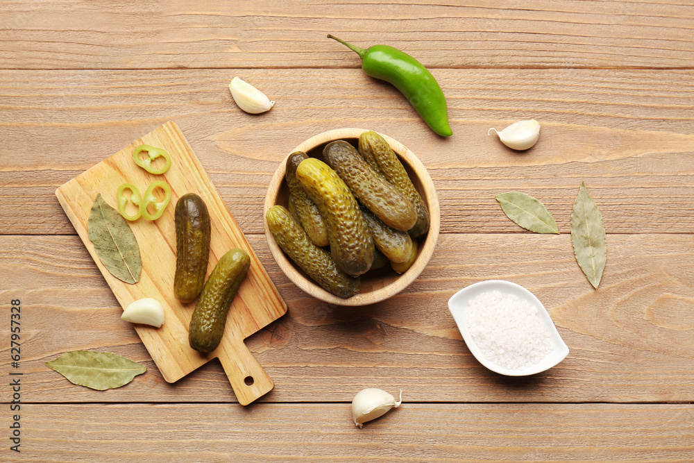 Bowl and board with pickled cucumbers on wooden background