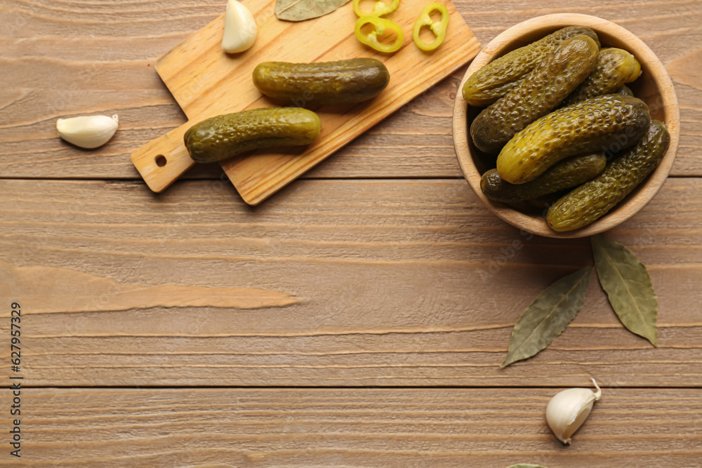 Bowl and board with pickled cucumbers on wooden background