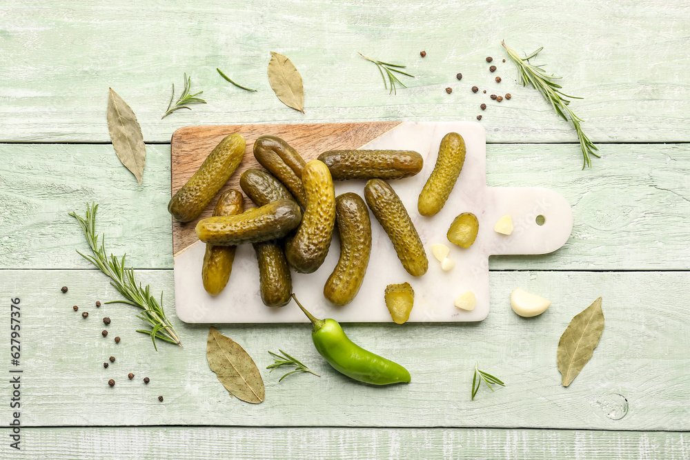 Board with pickled cucumbers and different spices on green wooden background