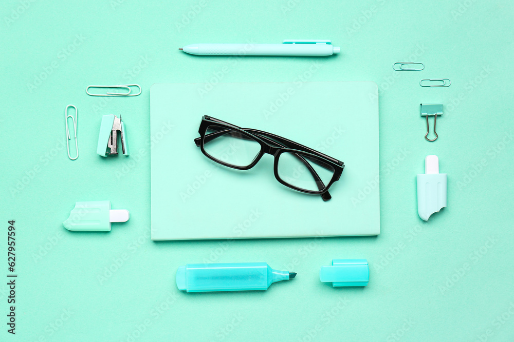 Stylish eyeglasses with stationery supplies on turquoise background