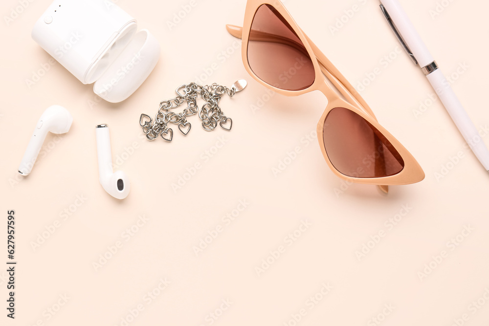 Stylish sunglasses with earphones and chain bracelet on pink background