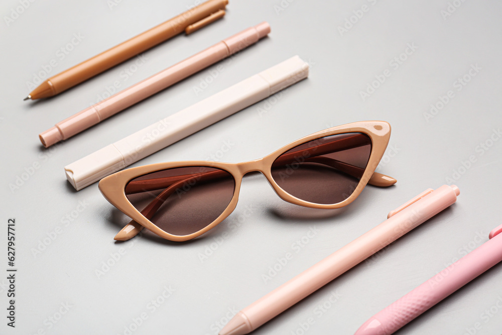 Stylish sunglasses with stationery supplies on grey background