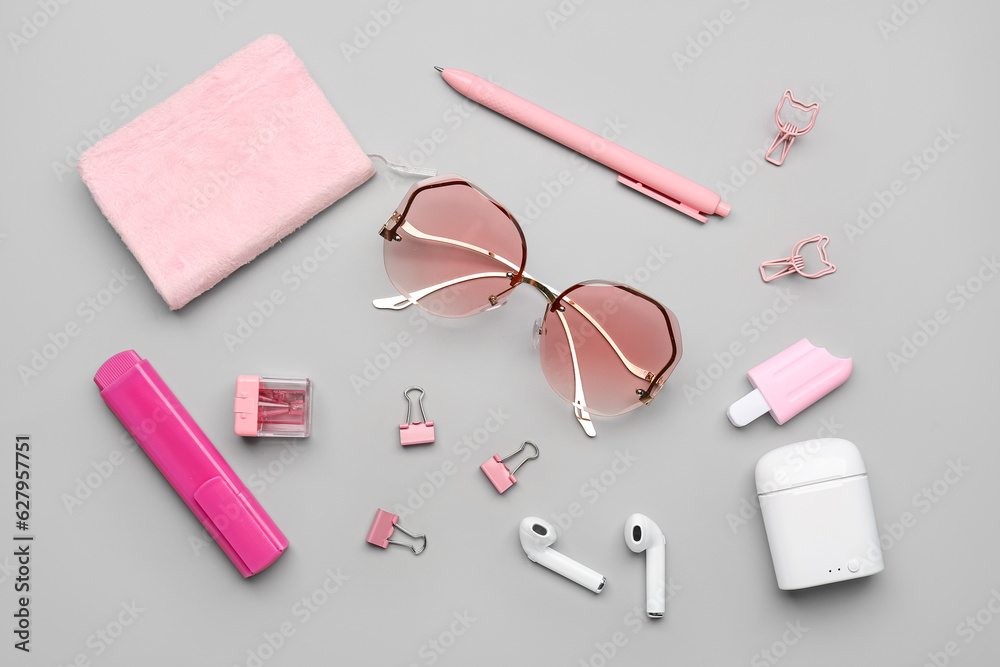 Stylish sunglasses with stationery supplies and earphones on grey background