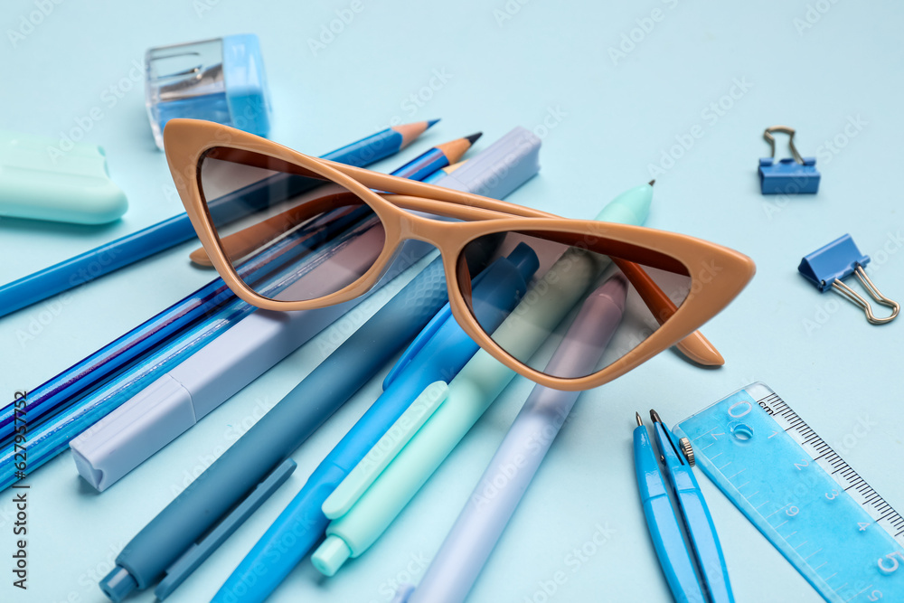 Stylish sunglasses with stationery supplies on blue background