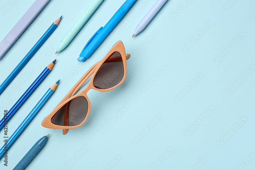 Stylish sunglasses with stationery supplies on blue background