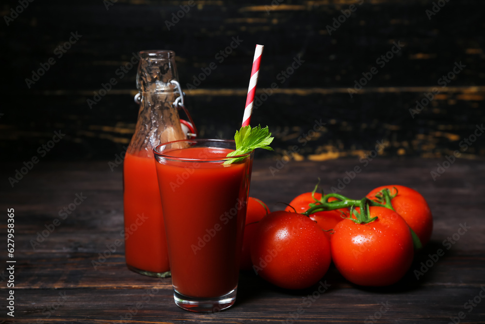 Glass and bottle of tasty tomato juice on black wooden background