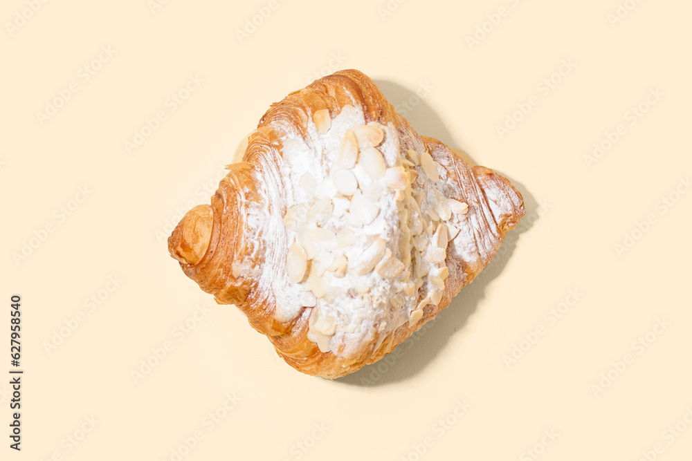 Sweet croissant with powdered sugar and nuts on beige background