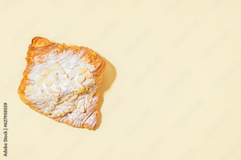 Sweet croissant with powdered sugar and nuts on beige background