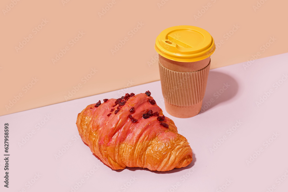 Sweet croissant and paper cup of coffee on pink table