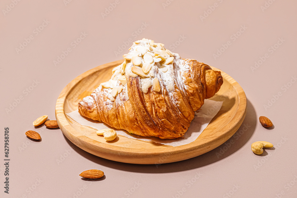 Wooden plate of sweet croissant with powdered sugar and different nuts on pink background