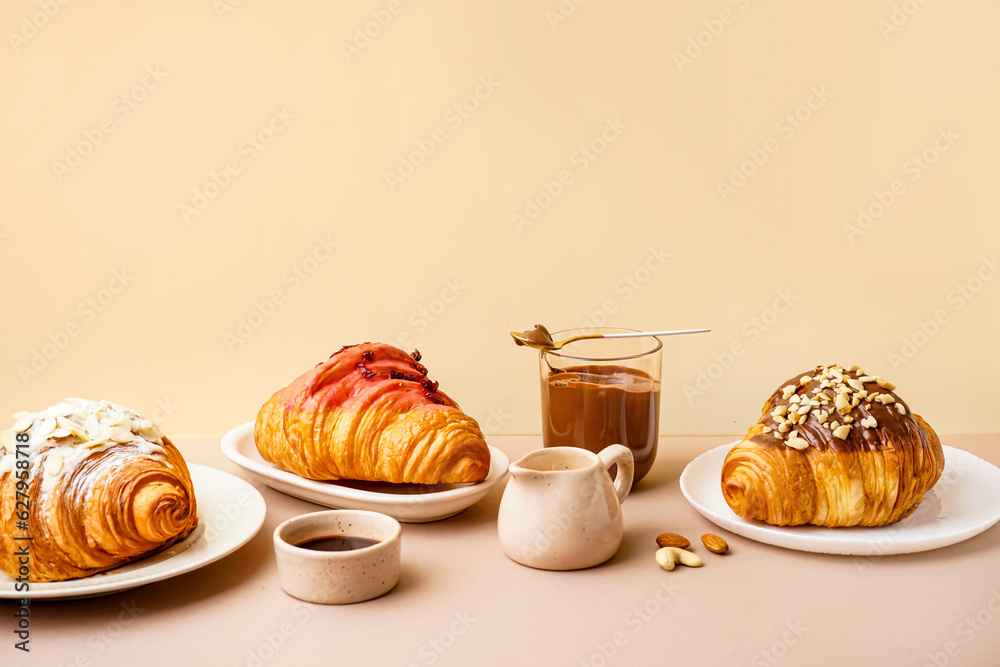 Plates with different sweet croissants and glass of chocolate on beige background