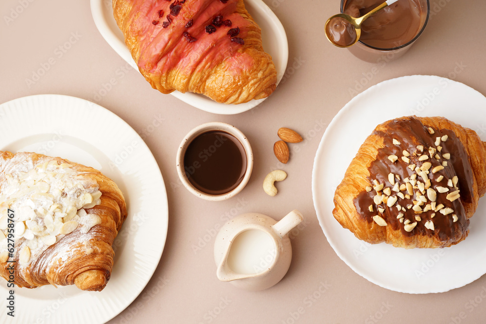 Plates with different sweet croissants and glass of chocolate on beige background