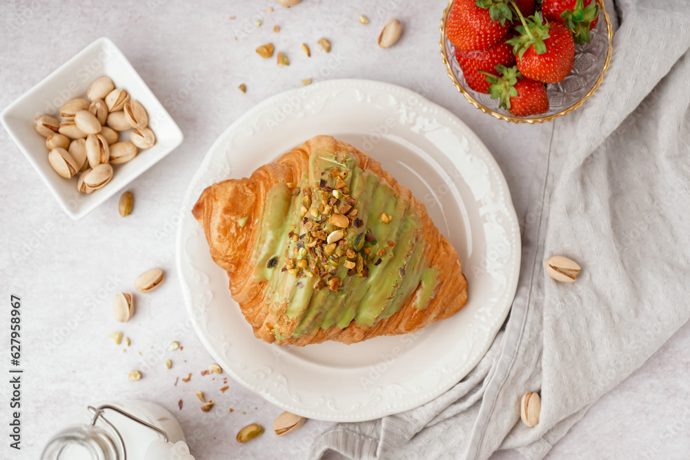 Plate with sweet croissant and pistachio nuts on white background