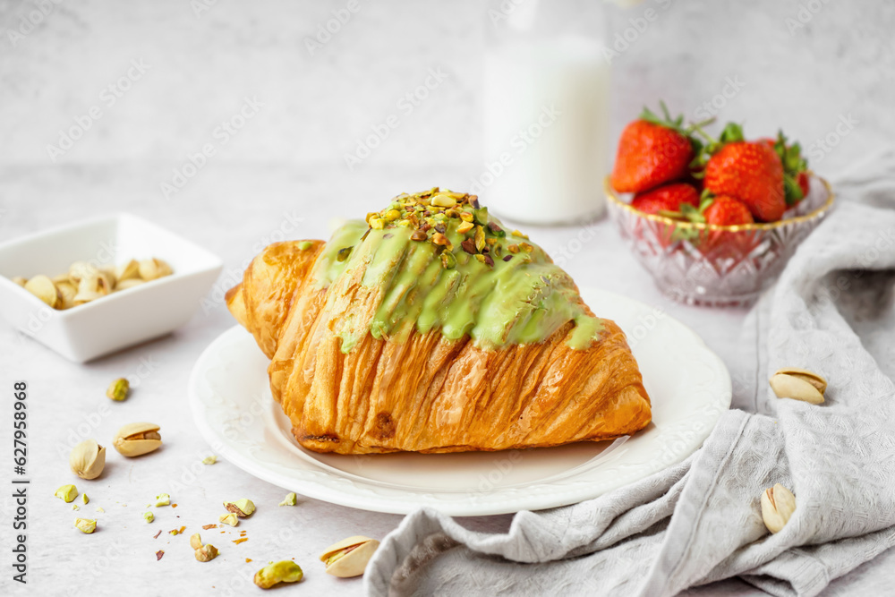 Plate with sweet croissant and pistachio nuts on white background