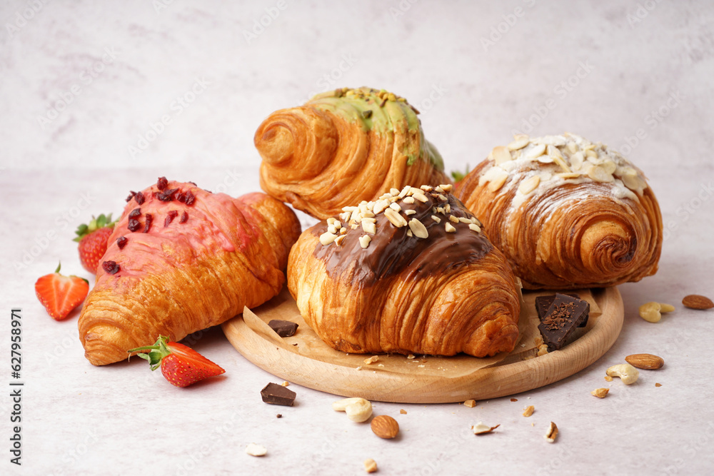 Wooden board with different sweet croissants and strawberries on white background