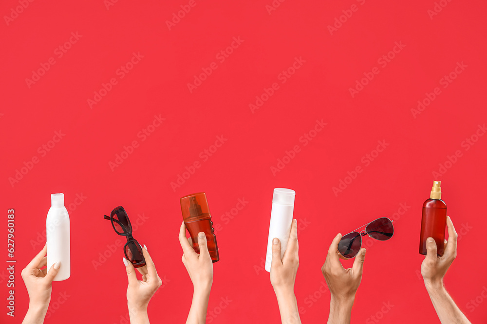 Female hands with bottles of sunscreen cream and sunglasses on red background