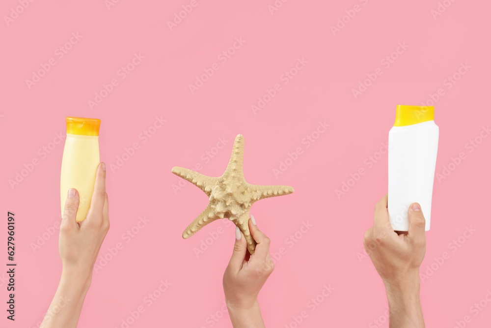 Female hands with bottles of sunscreen cream and starfish on pink background