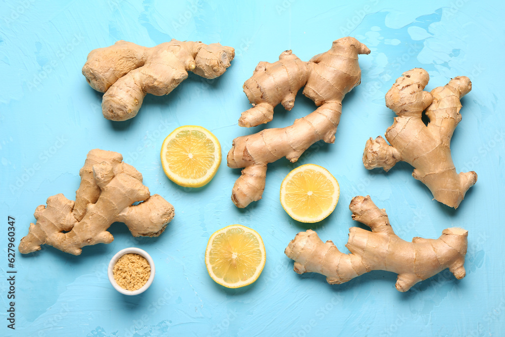 Fresh ginger roots, slices of lemon and bowl of dried powder on blue background