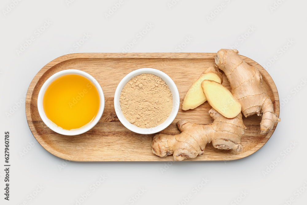 Wooden board with fresh ginger root, honey and bowl of dried powder on grey background