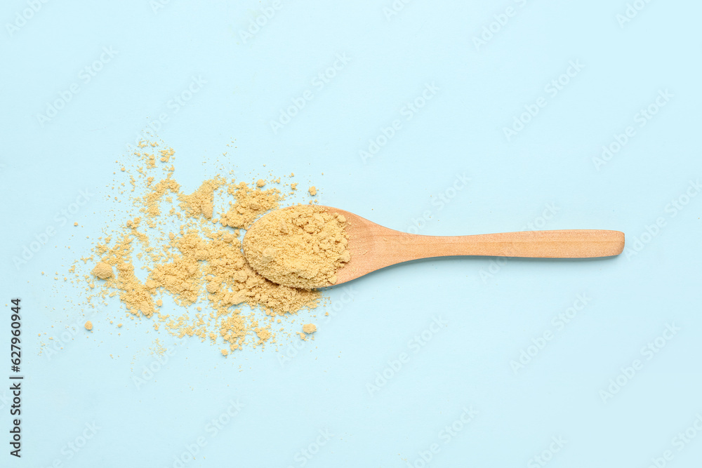 Wooden spoon with ginger powder on blue background